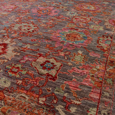 A close-up of a floral area rug with a distressed pattern in muted tones of sage green, rose pink, heather, blue, pale green and terracotta.