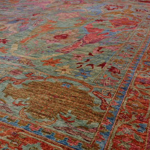 A close-up view of an ornate traditional area rug with a complex floral and medallion pattern in muted tones of sage green, terracotta red, dusty blue, and golden brown.